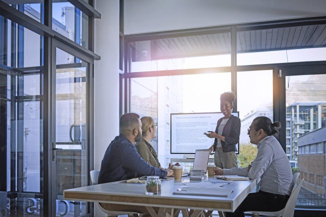 Geschäftsleute in einem Meeting, bei dem eine Dame vor der Gruppe präsentiert