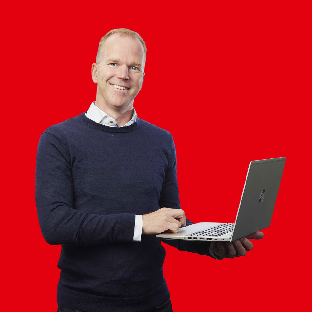 Mann mit blauem Pullover und weißer Bluse lächelnd mit einem Laptop