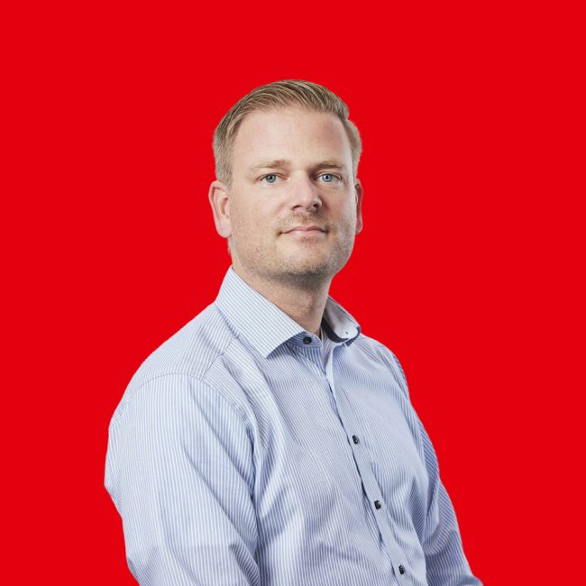 Mann mit blonden Haaren und hellblauer Bluse schaut in die Kamera